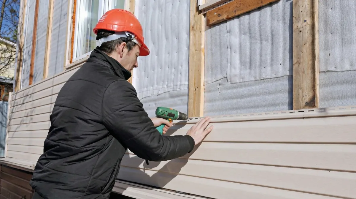 Siding replacement professional using a power drill to install new tan vinyl siding on a home exterior in Colorado Springs, CO